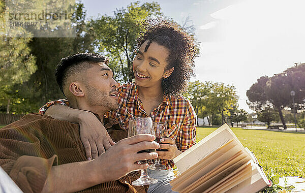 Young man holding wine glass and sitting with girlfriend at public park