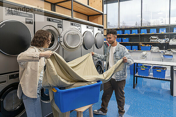 Young couple folding sheet together in laundromat