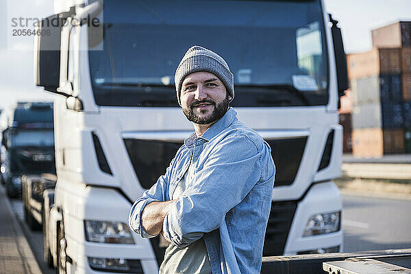 Thoughtful truck driver standing with arms crossed in front of truck