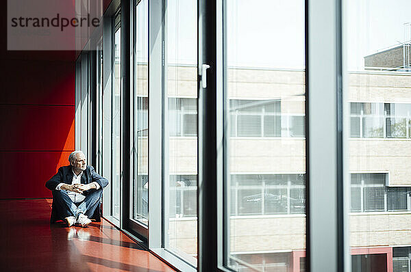 Businessman with legs crossed looking out through office window