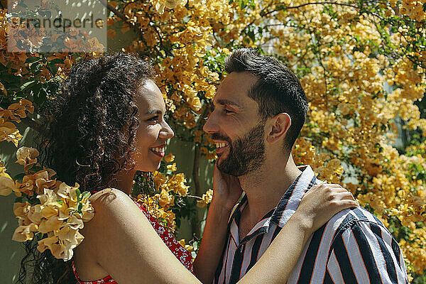 Happy multiracial couple standing near bougainvillea vine