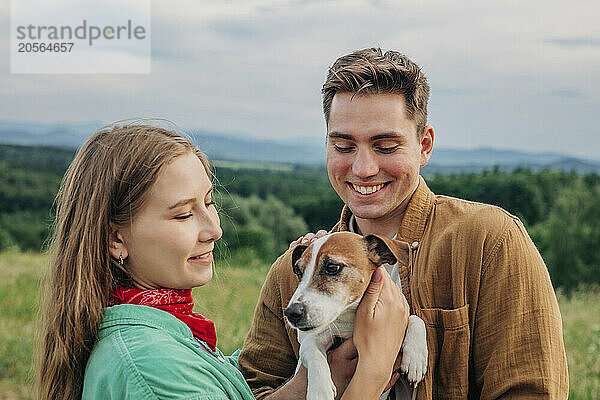 Smiling young couple playing with dog on mountain of Poland