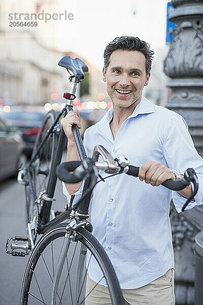 Smiling handsome mature businessman carrying bicycle