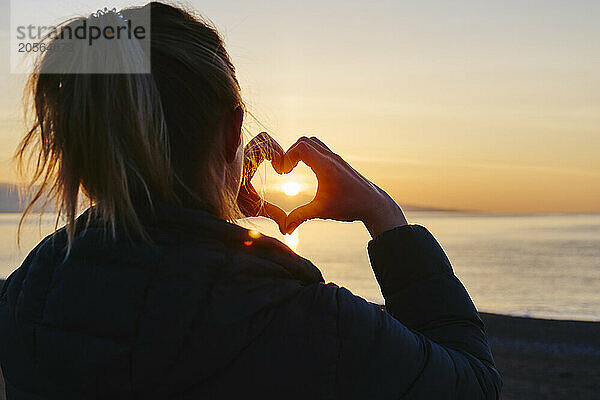 Woman making heart shape during sunrise at beach