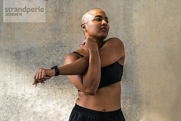 Active sportswoman stretching arms in front of wall