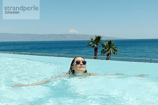 Happy woman enjoying in swimming pool next to sea on sunny day