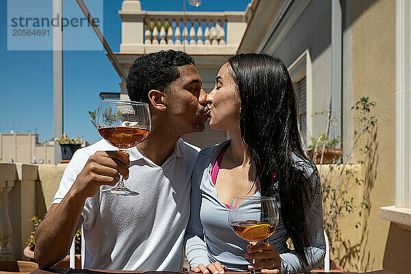 Affectionate young couple with drinks kissing on sunny day