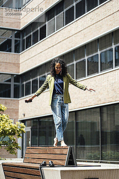 Businesswoman balancing and walking with arms outstretched on bench at office park