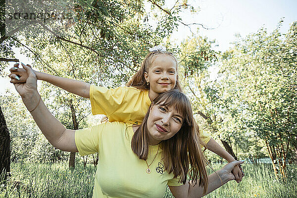 Smiling mother giving piggyback ride to daughter in garden