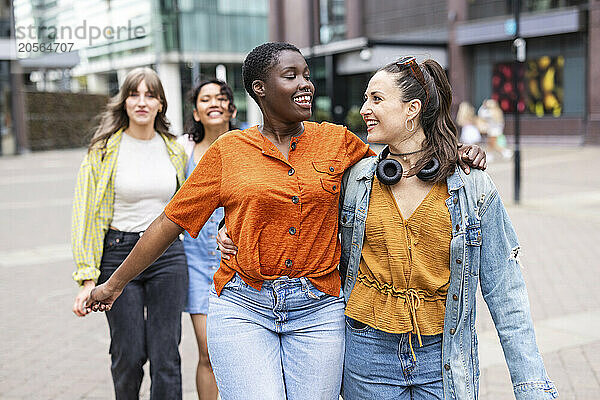 Happy women walking with arms around in city