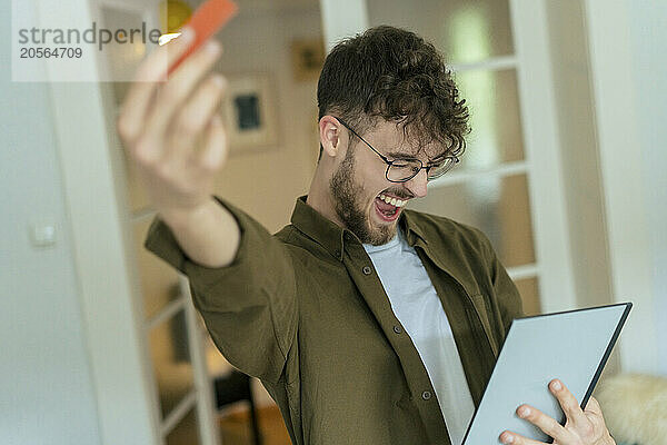 Excited young man with tablet PC standing at home