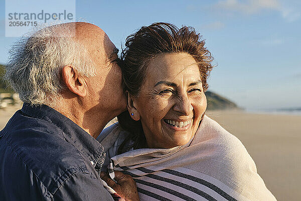 Senior man kissing and embracing woman at beach on sunny day