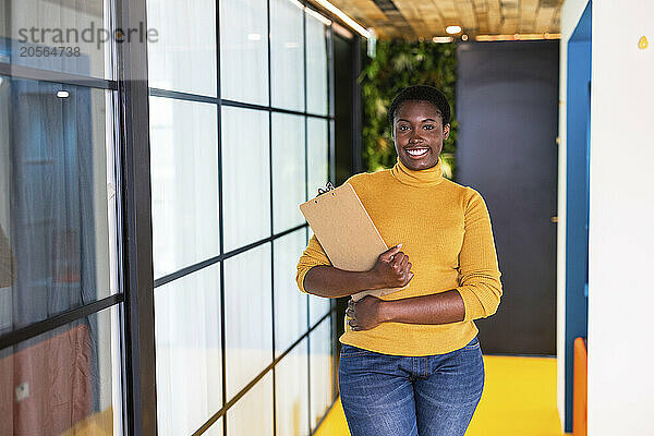 Confident businesswoman holding clipboard and standing in office