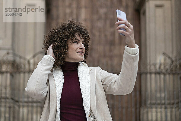 Woman with hand in hair taking selfie through smart phone