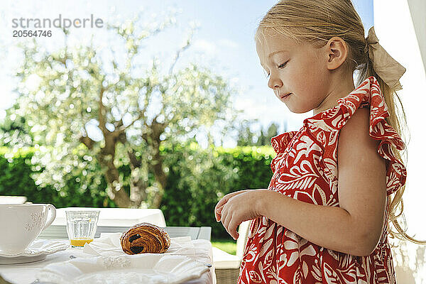 Blond girl looking at croissant on table