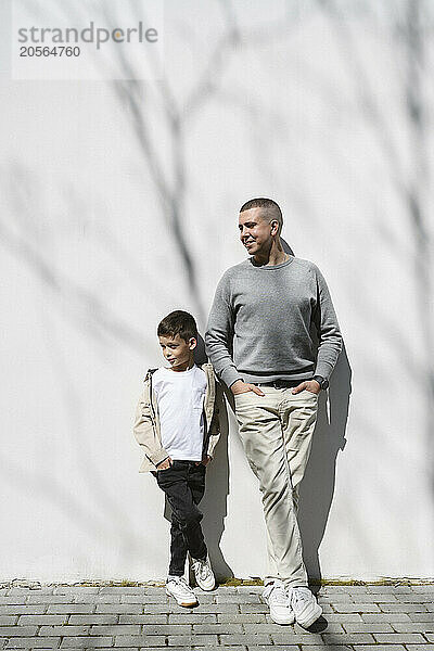 Man with hands in pockets standing with son near wall