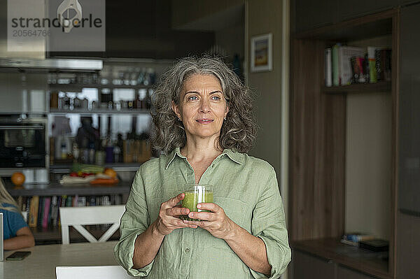 Thoughtful gray hair woman holding smoothie glass at home