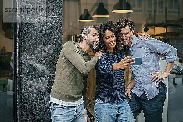 Smiling business colleagues taking selfie in front of cafe