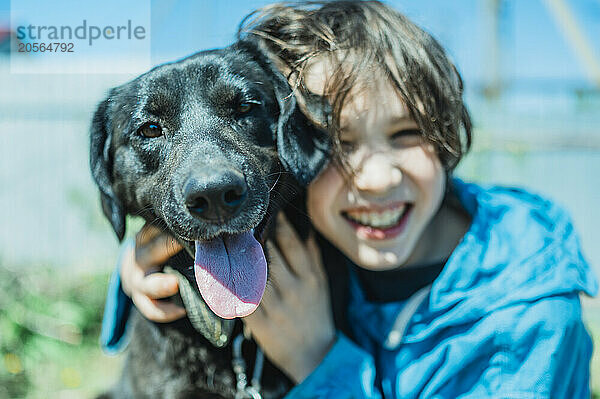 Cheerful boy embracing dog on sunny day