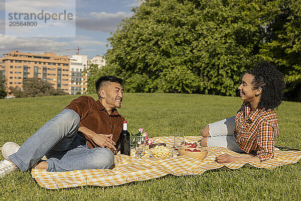 Happy boyfriend and girlfriend lying on picnic blanket in public park