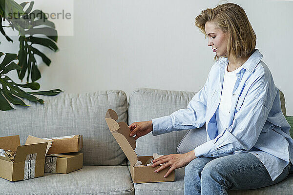 Young woman opening delivery box sitting on sofa at home