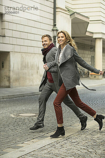 Happy couple holding hands and crossing street in city