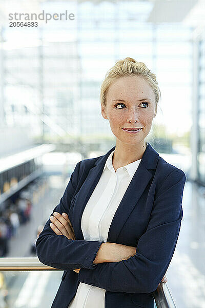 Smiling businesswoman leaning with arms crossed on railing in airport lobby