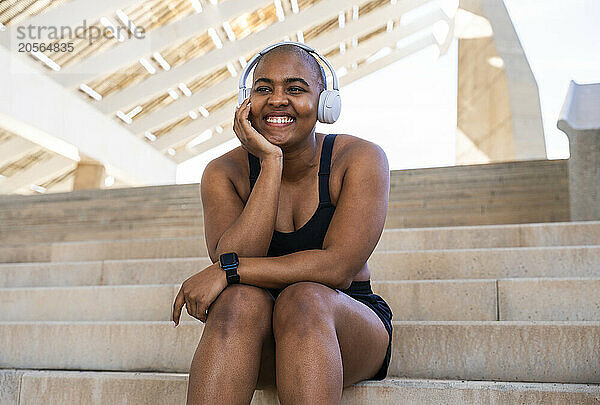 Happy muscular woman wearing headphones sitting on steps