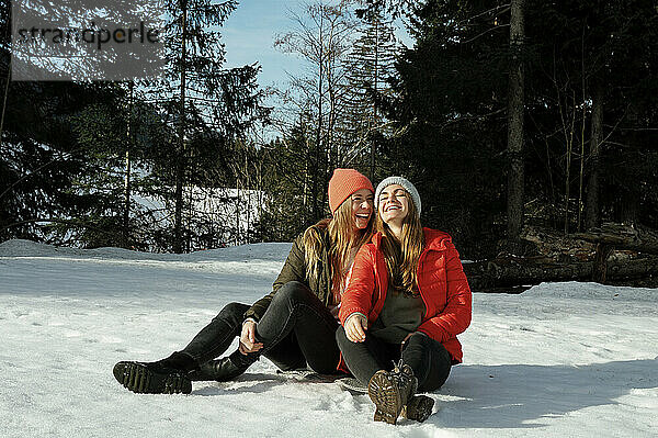 Happy friends sitting on snow field enjoying vacation