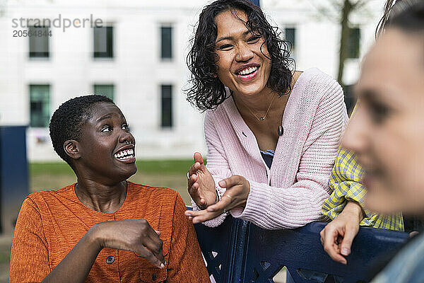 Cheerful woman leaning on bench talking with friends at park