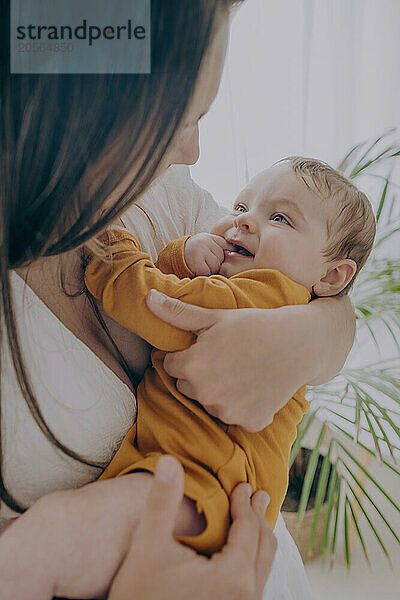 Young mother carrying baby boy in arms at home