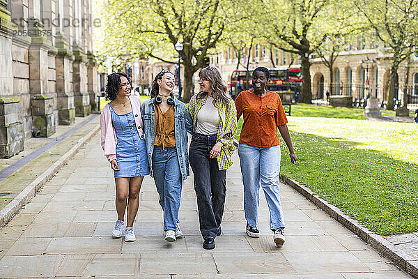 Happy multiracial female friends walking together on footpath