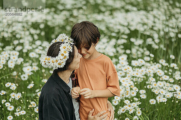 Mother wearing daisy wreath hugging son in field