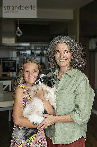 Happy mother and daughter standing with dog at home