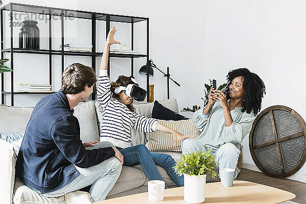 Family sitting on couch mother taking pictures of daughter using virtual reality simulator