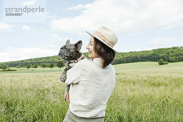 Happy woman carrying french bulldog in green field