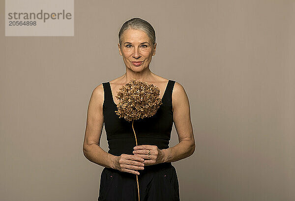 Senior woman holding dead plant against brown background