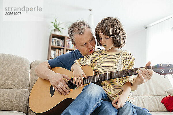 Son learning guitar with father at home