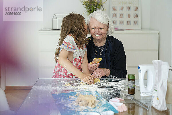 Girl whispering in grandmother's ear and kneading dough