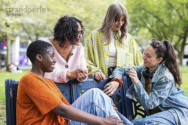 Happy woman sitting on bench talking with friends at park