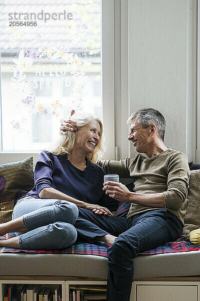 Happy retired senior couple sitting on alcove window seat at home