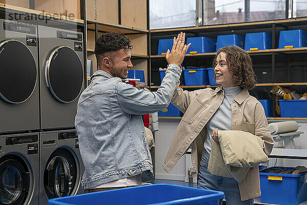 Happy young couple giving high-five at laundromat