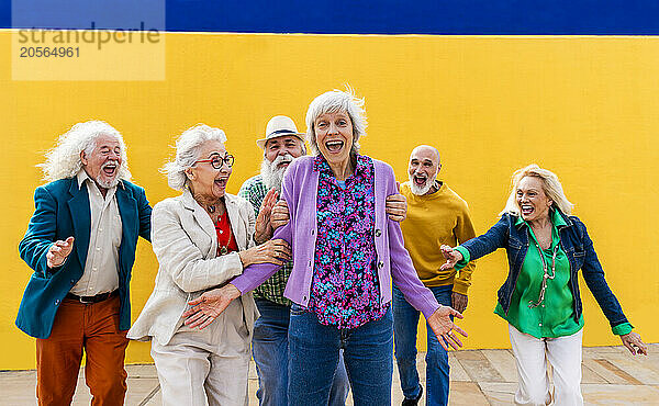 Playful senior men and women catching cheerful friend on footpath