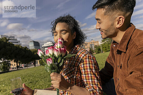 Young woman smelling flowers and sitting with boyfriend at park