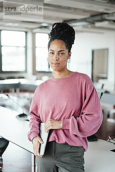 Confident beautiful young businesswoman with laptop standing at workplace