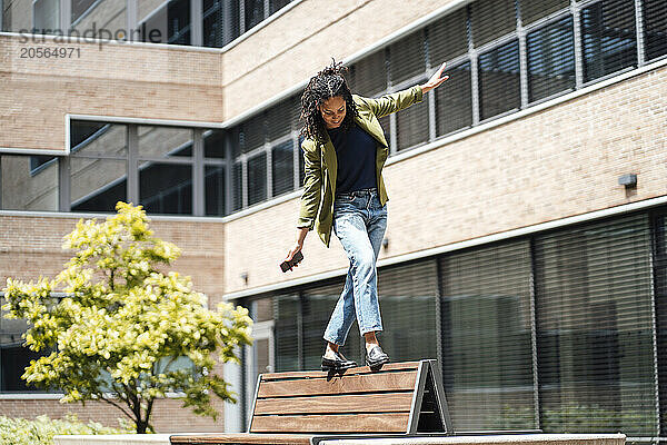 Young businesswoman balancing and walking on bench at office park