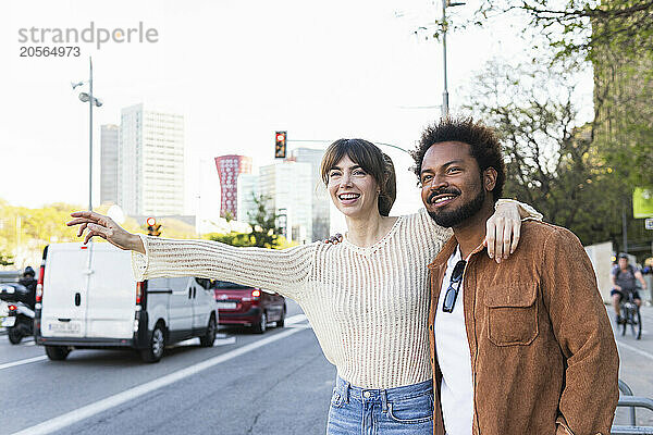 Happy woman with arm around boyfriend hailing ride at roadside in city