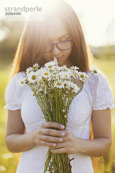 Young woman smelling bunch of chamomile in field