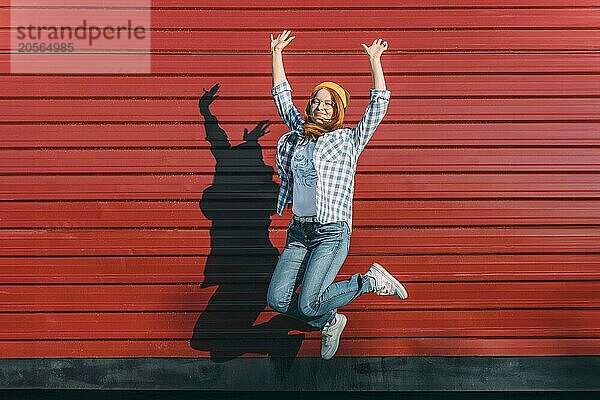 Cheerful teenage girl jumping in front of corrugated iron