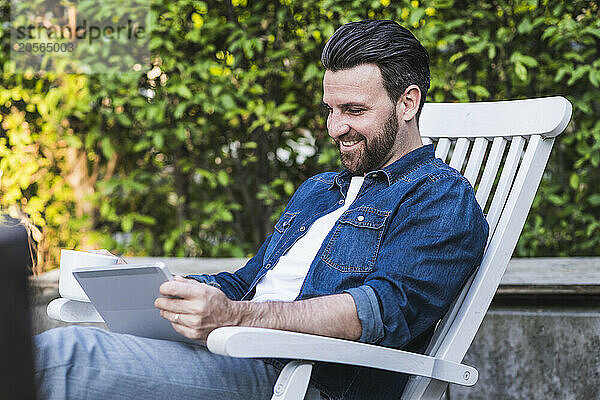 Happy man using tablet PC on chair